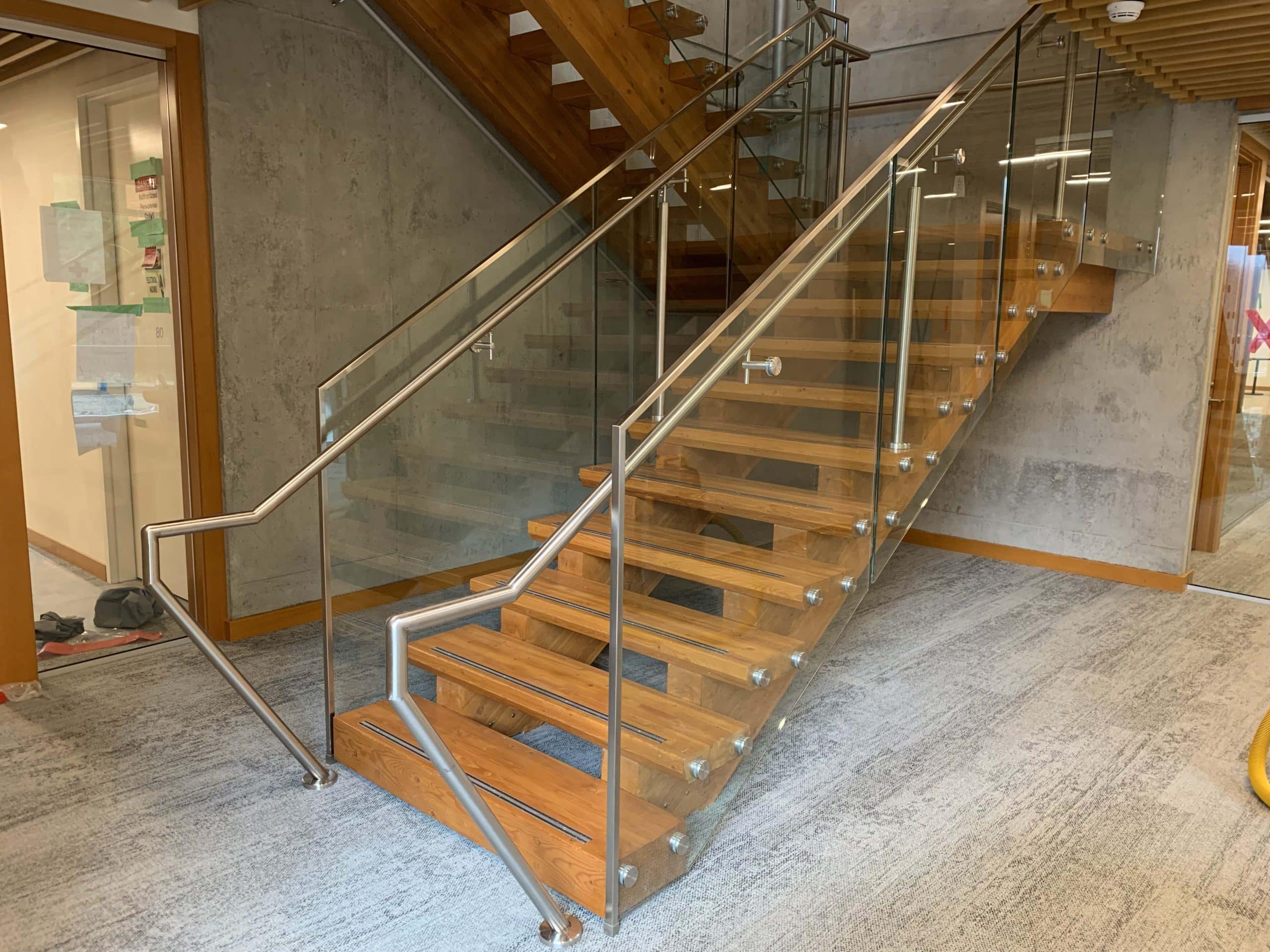 A modern staircase with glass railings and wooden handrails.